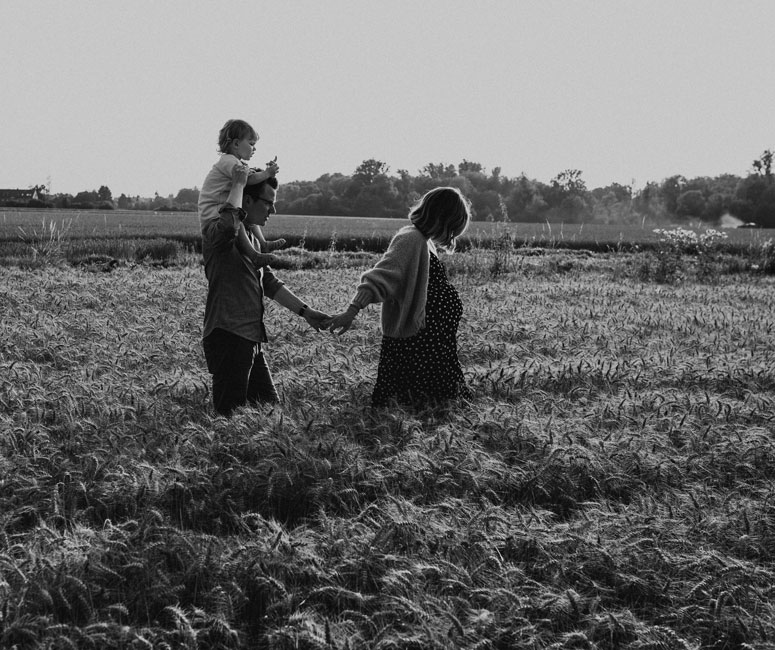 Ein Vater mit Kind auf der Schulter und seiner Frau an der Hand laufen durch ein Feld. Dokumentarische Familienfotografie in der Natur nähe Düsseldorf.
