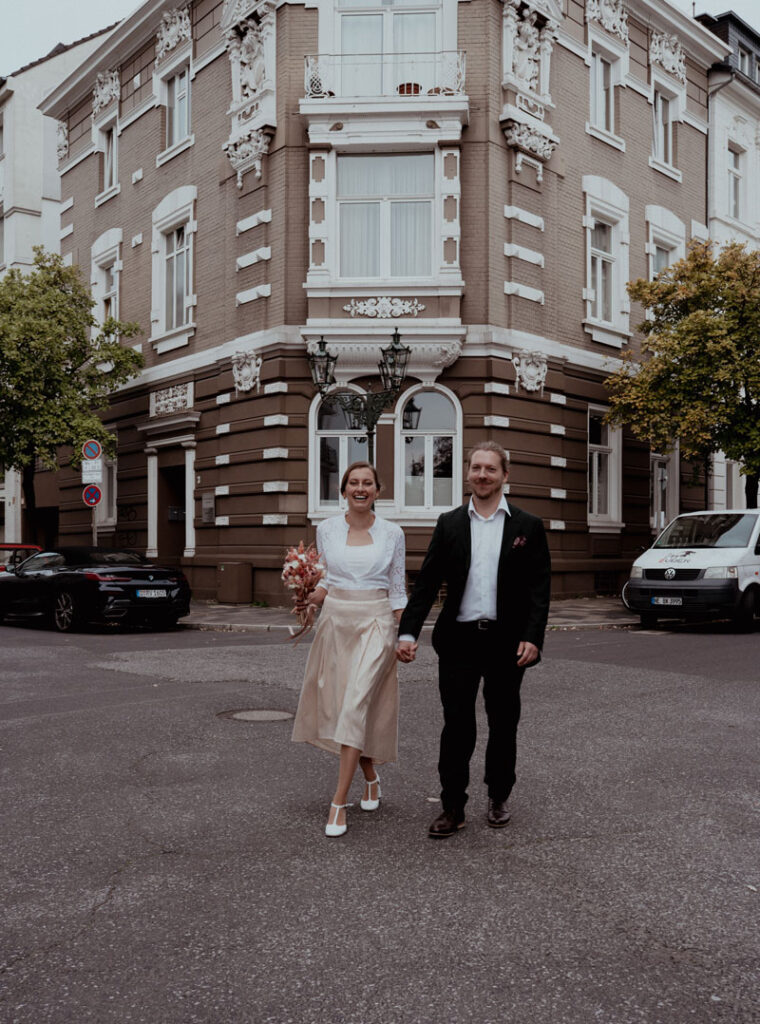 Brautpaar überkreuzt die Straße in Düsseldorf und halten Ihre Hand. Aufgenommen von Alina Lowe