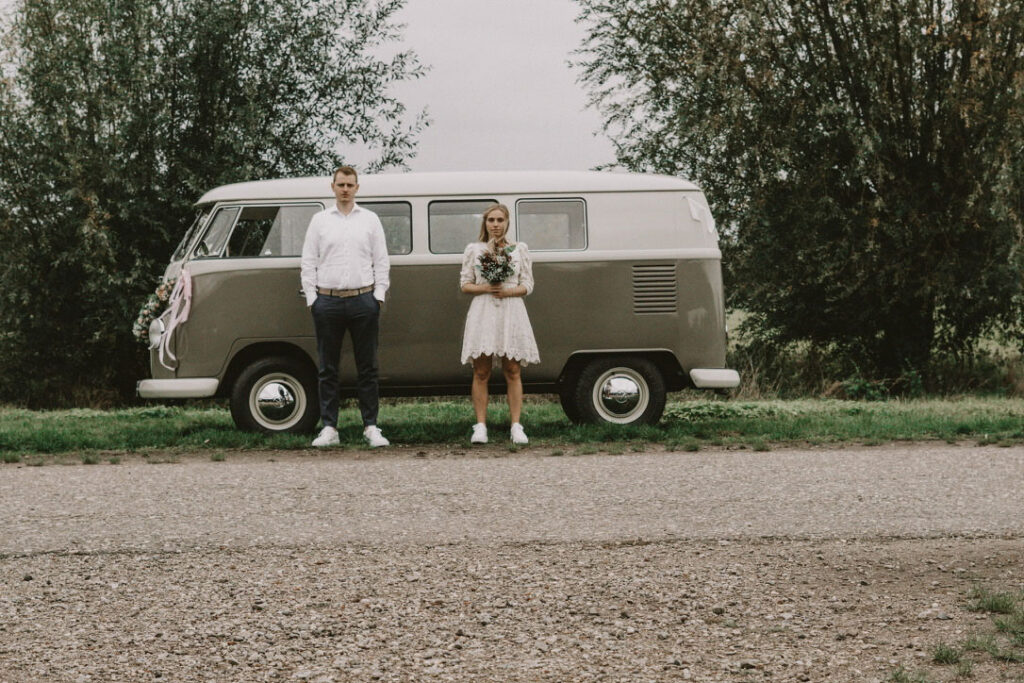 Brautpaar mit Brautstrauß in der Hand steht vor einem VW Bulli T2 in Köln.